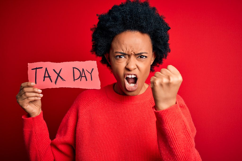 An angry, frustrated woman holds up a sign that says "tax day."