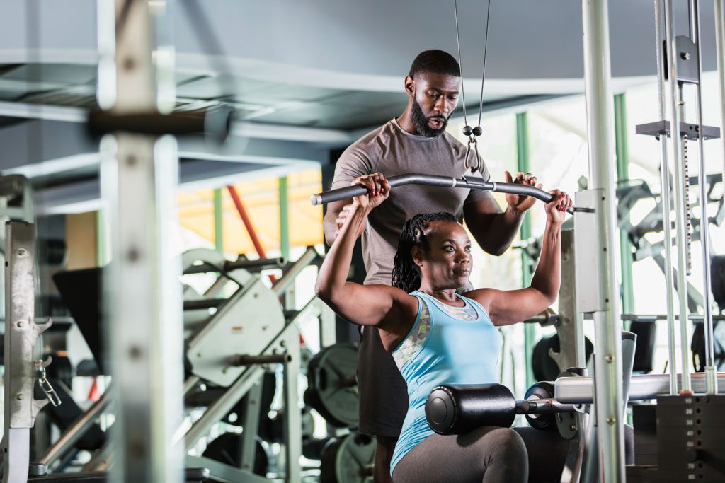 A personal trainer spots a client on a seated lat-pulldown machine.