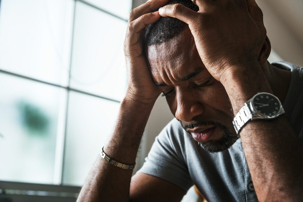 A closeup image of a very stressed man with his hands on his head.