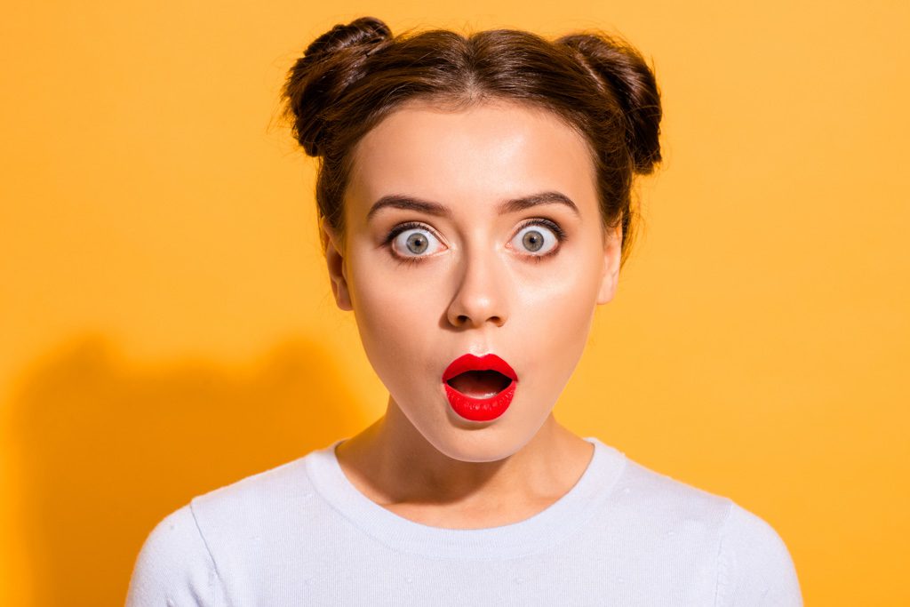 A portrait of a shocked woman in front of an orange background.