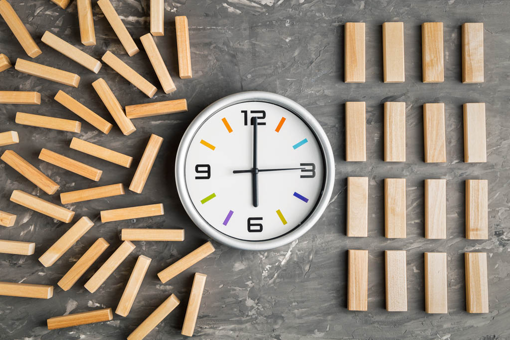 A jumbled pile of wooden blocks and a carefully organized pile sit on opposite sides of a clock.