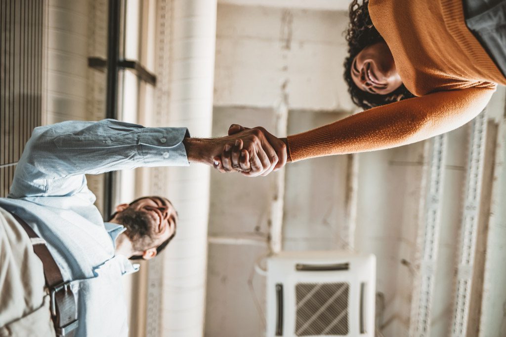 A gym owner shakes hands with a prospective client who has arrived for a free consultation.