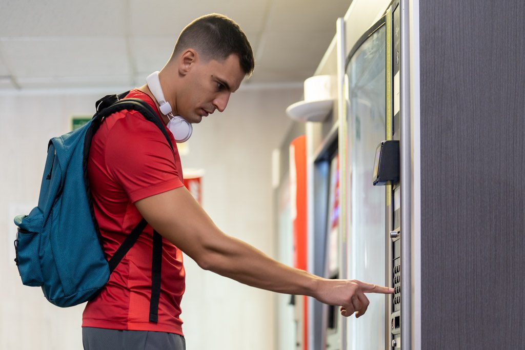 A man at a gym makes a purchase from a vending machine.