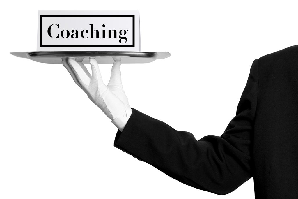 A hand wearing a white glove holds a silver tray with a card that reads "coaching" in elegant script.
