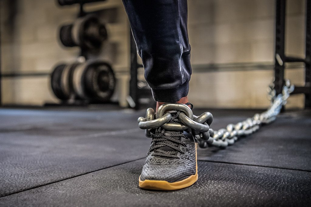 In a gym, the owner's leg is chained to a squat rack, preventing forward movement.
