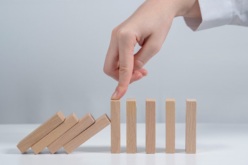 A closeup of a finger stopping a sequence of dominoes from continuing to demonstrate stalled progress.