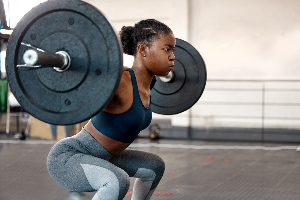 A woman performs a barbell back squat to build strength in a functional fitness gym.