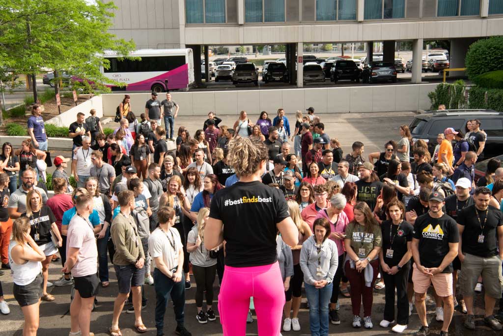 A photo of a woman in a shirt that reads "best finds best" organizing a large group photo at the 2023 Two-Brain Summit in Chicago.