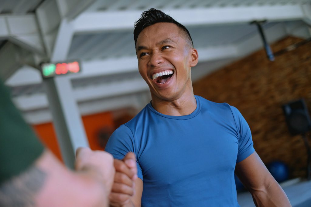A smiling fitness coach bumps fists with a personal training client in a gym.