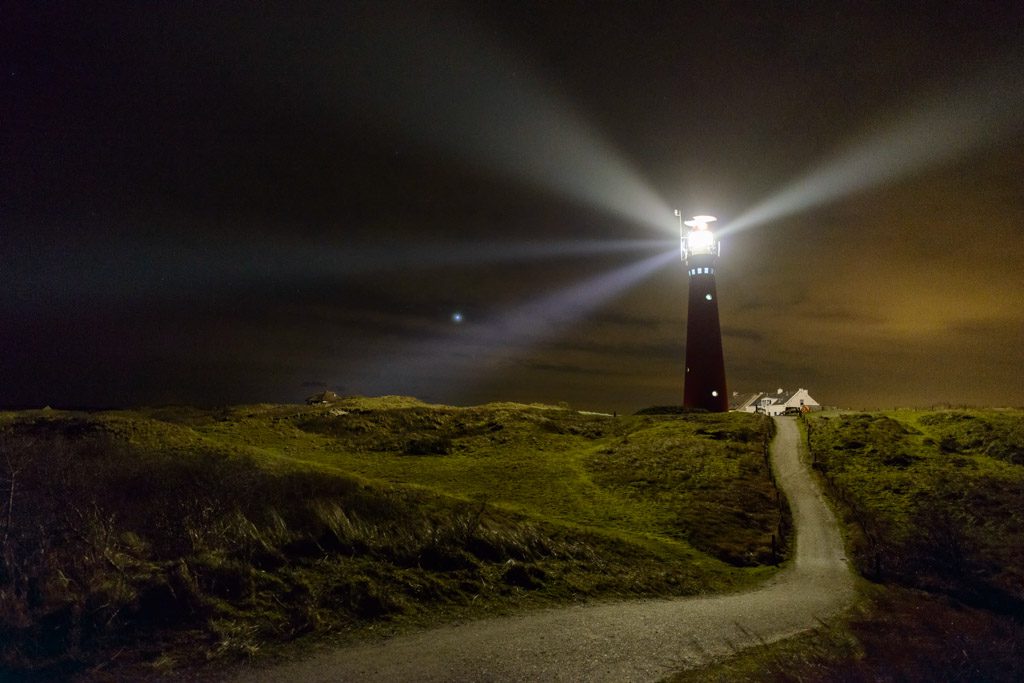 Lighthouse and fishermen's cottages in the night on an island in The Netherlands. A path is leading up the dunes towards a lighthouse.