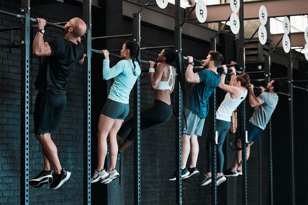 Six gym members perform pull-ups in a group class at a functional fitness facility.