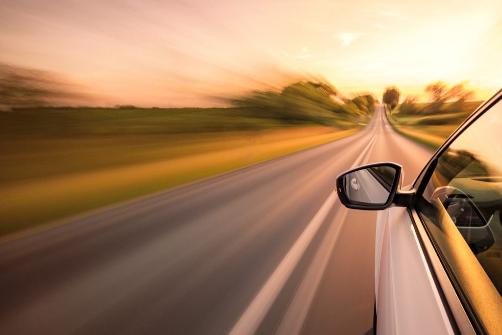 A photo of a car speeding down an open highway at sunset.