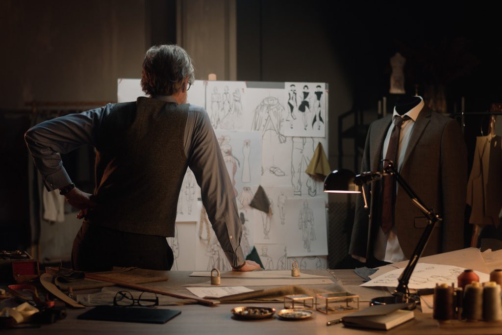 A tailor stands in his workshop and reviews designs for clothing.