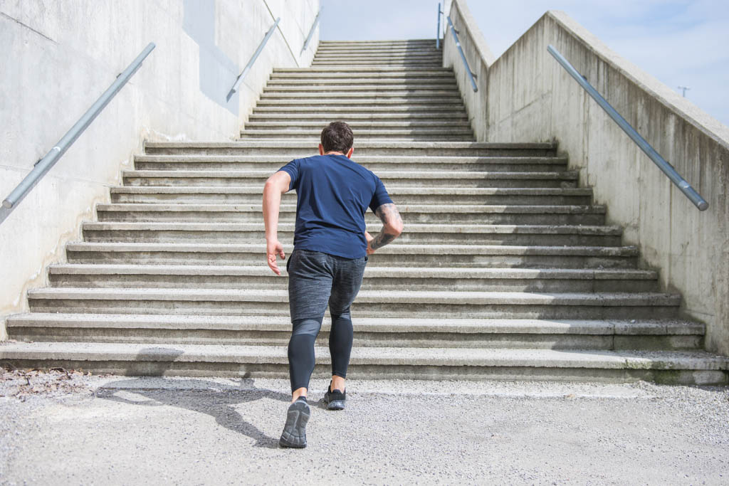 A man in athletic apparel prepares to run up a long flight of concrete stairs.