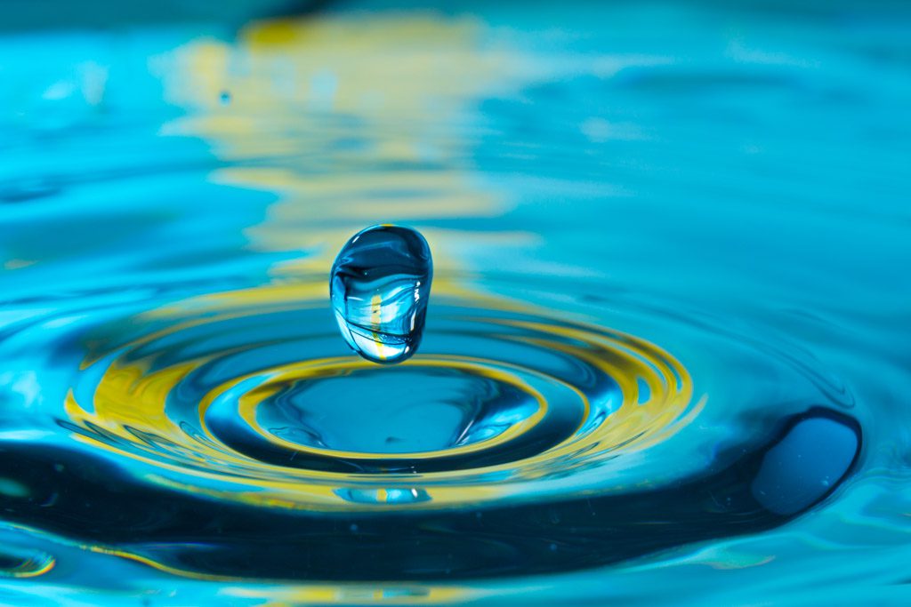 A single drop of blue water just about to make an impact in a deep blue pond.