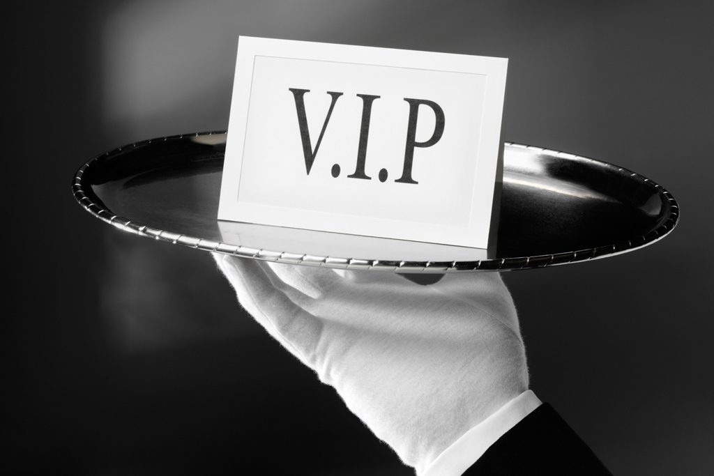 A close-up image of a white-gloved hand holding a silver platter with a card labeled "VIP."