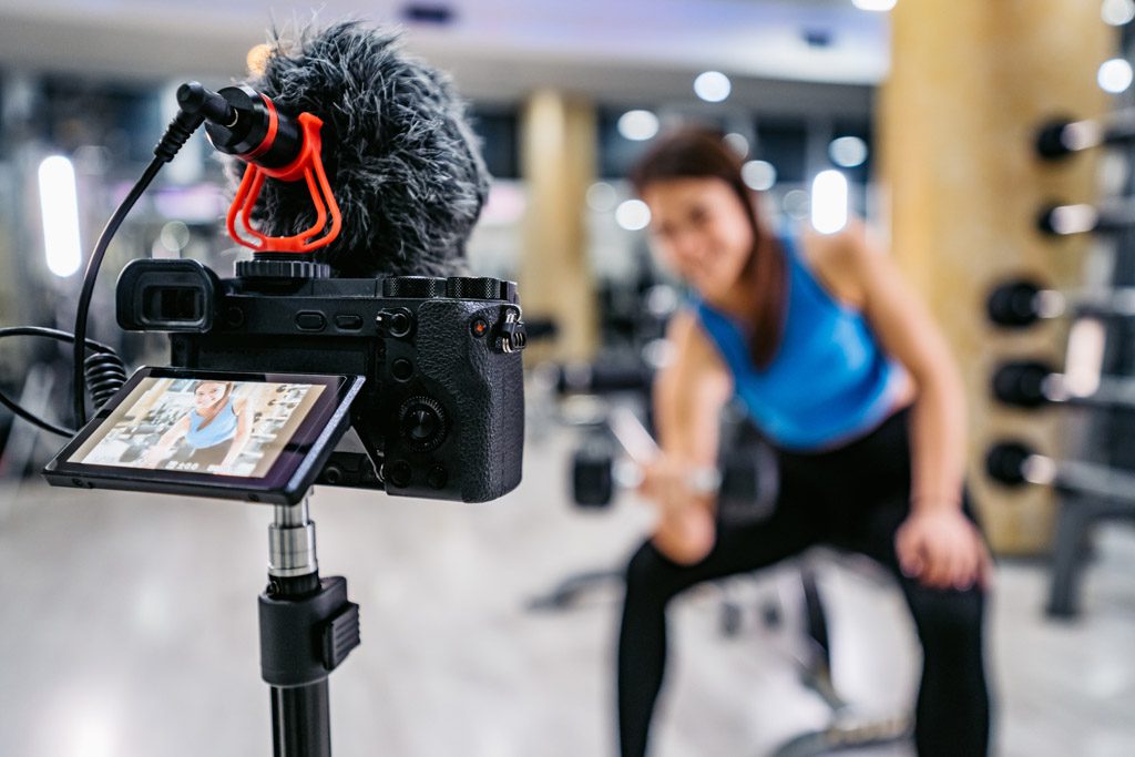 A photograph from behind a camera as a gym owner makes a video about the value of biceps curls.