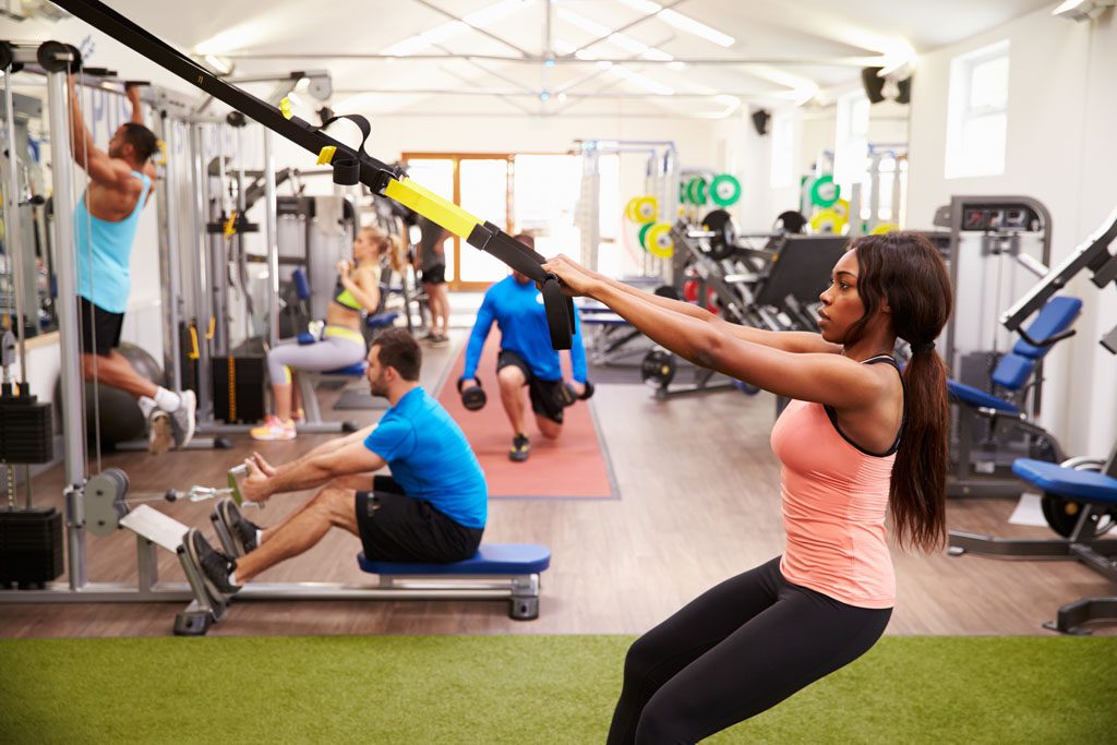 A group of people work out with assorted equipment in a busy gym.