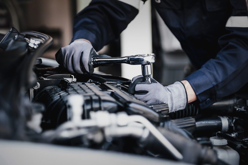 A closeup picture of a mechanic using a ratchet to repair a car engine.