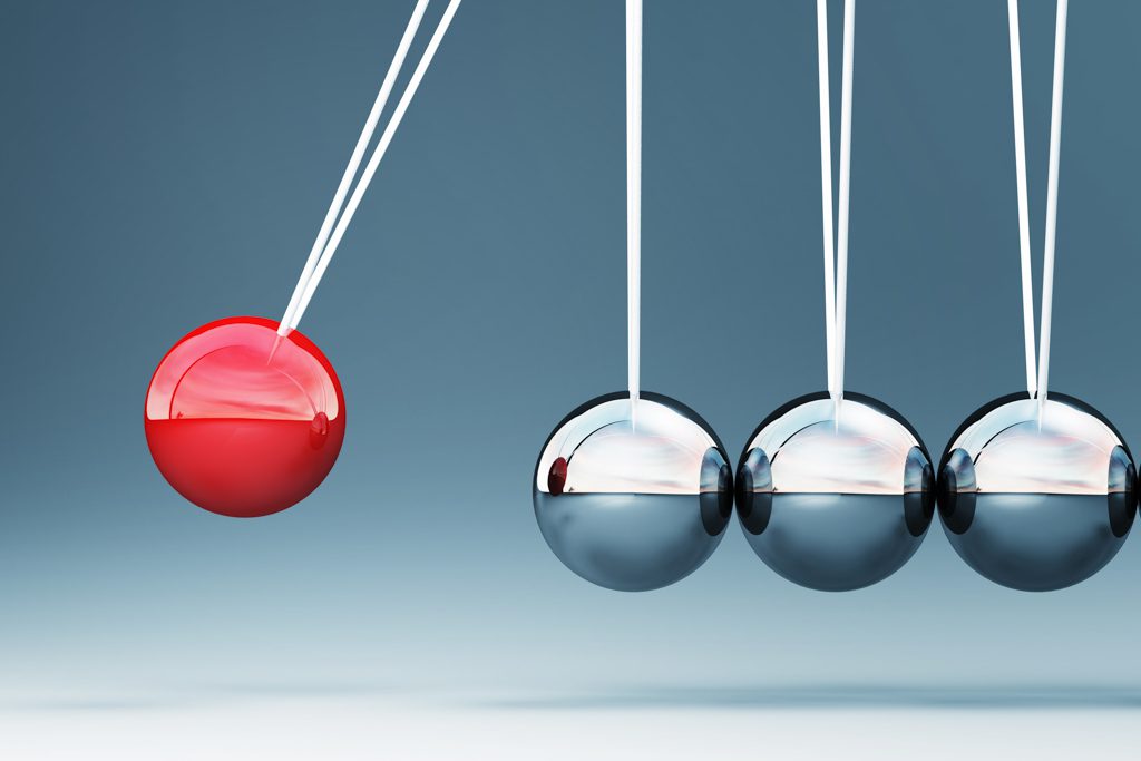 A closeup image of a Newton's cradle. The ball in motion is bright red.