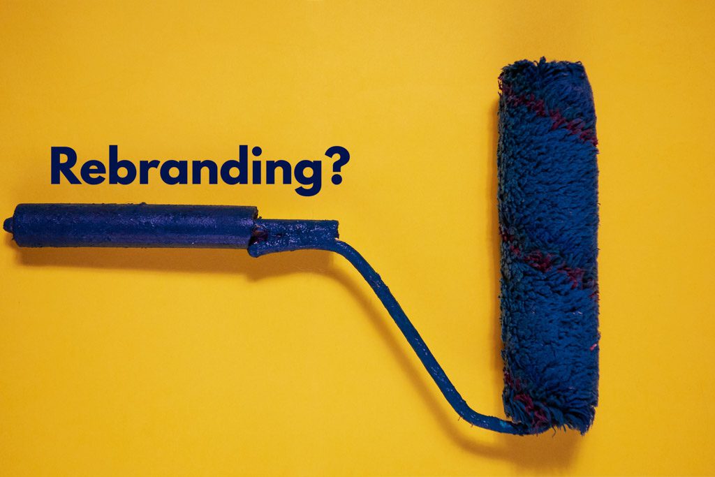 A bright blue paint roller on a yellow background with the word "rebranding?" on it.
