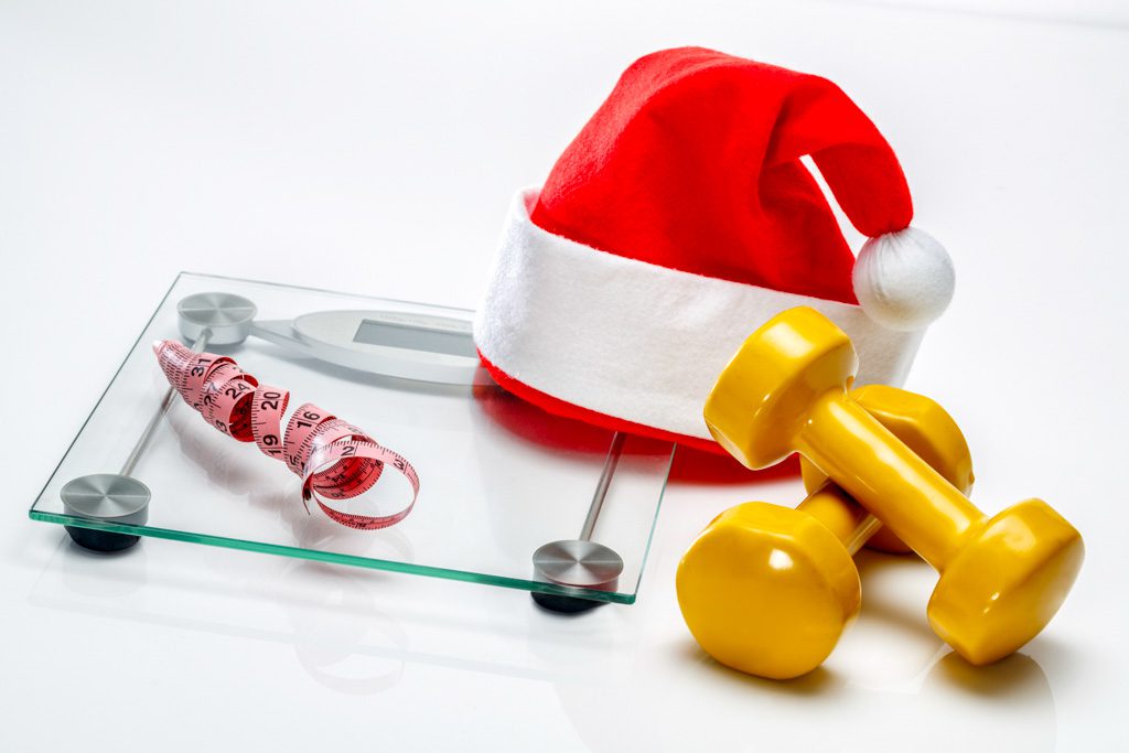 On a white background, a Santa hat, a scale, a measuring tape and gold dumbbells.