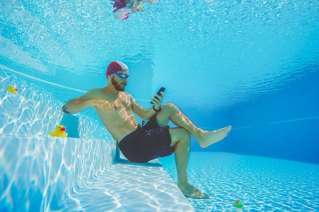 A man sits underwater and looks at social media on his smartphone.