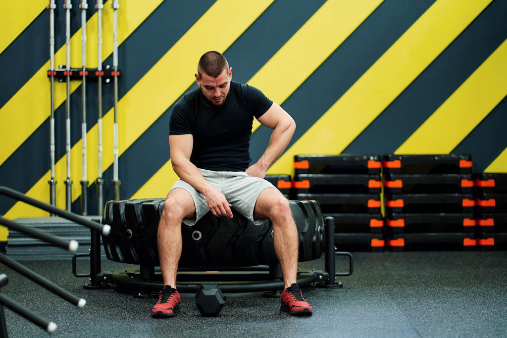 A dejected personal trainer sits on a tire in a functional fitness gym.