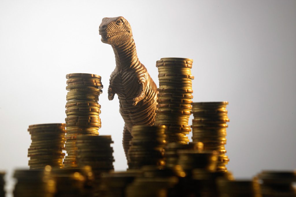 A giant T-rex dinosaur stands behind huge stacks of gold coins.