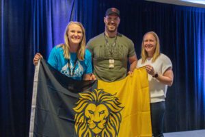 Two gym owners hold a lion flag and celebrate next to Two-Brain mentor Joleen Bingham.