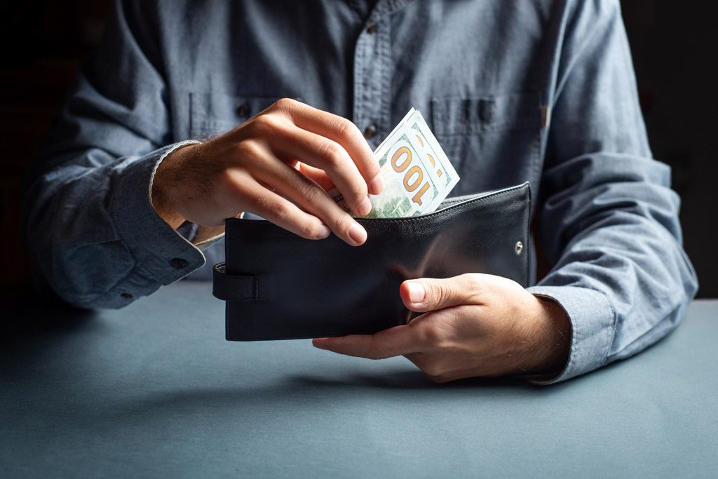 A closeup picture of a person taking hundred-dollar bills out of a black wallet.