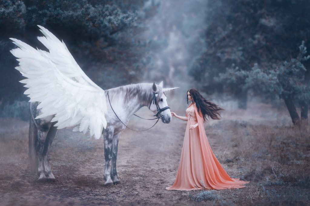 An elf in a peach dress pets a white, winged unicorn in a forest.