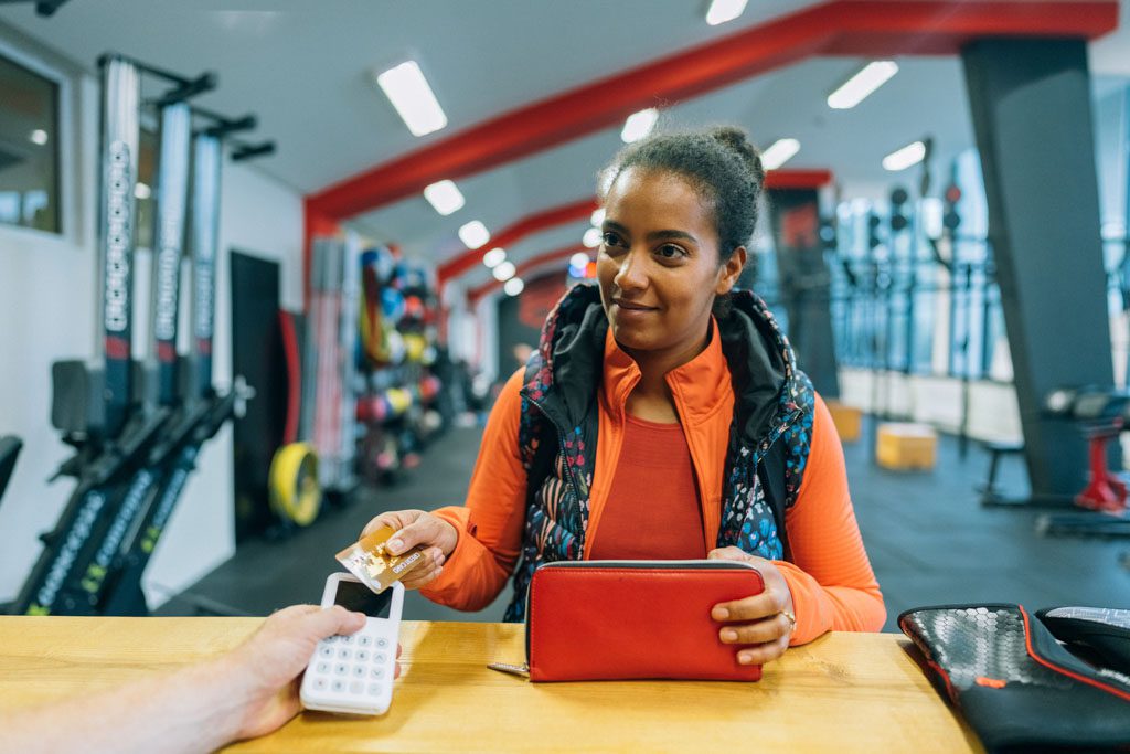 A gym client taps her credit card to pay for services at the front desk.