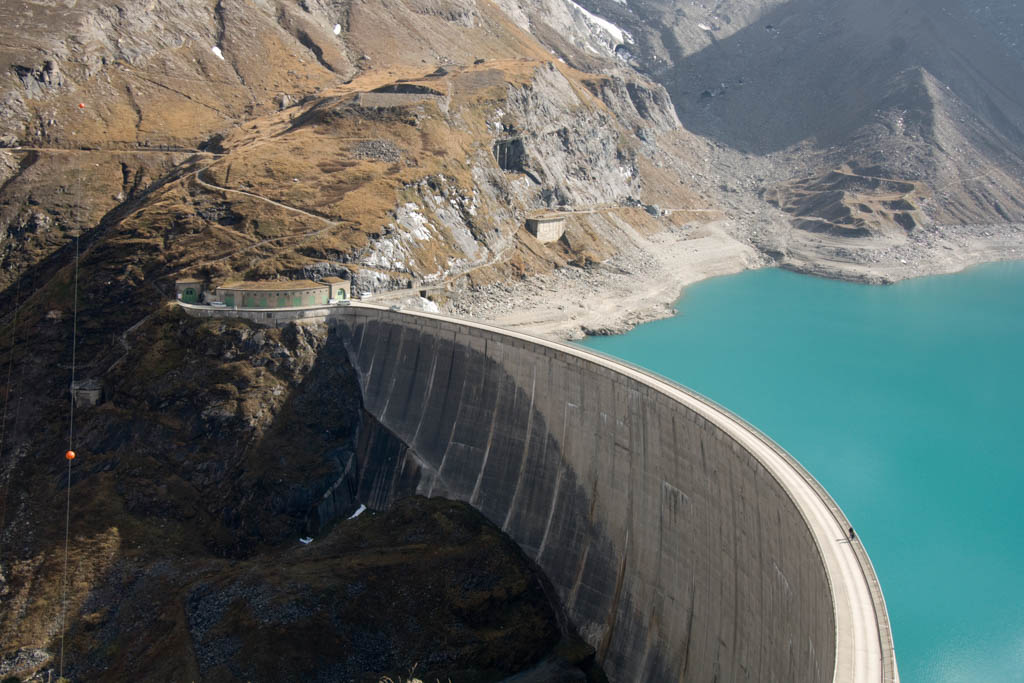 An aerial photo of a large dam holding back blue water in a reservoir.