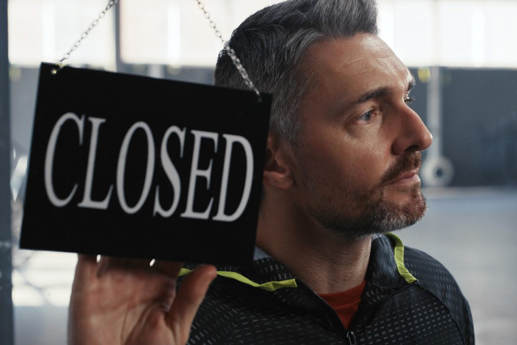 A sad gym owner flips his sign to "closed" as his business shuts down.