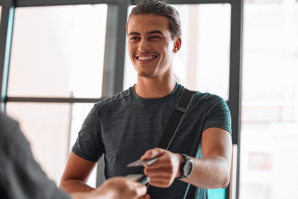 A smiling man hands his credit card to a gym owner to purchase a membership.