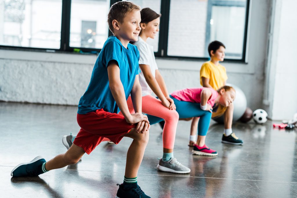 A group of kids perform lunges as part of a gym's summer fitness program.