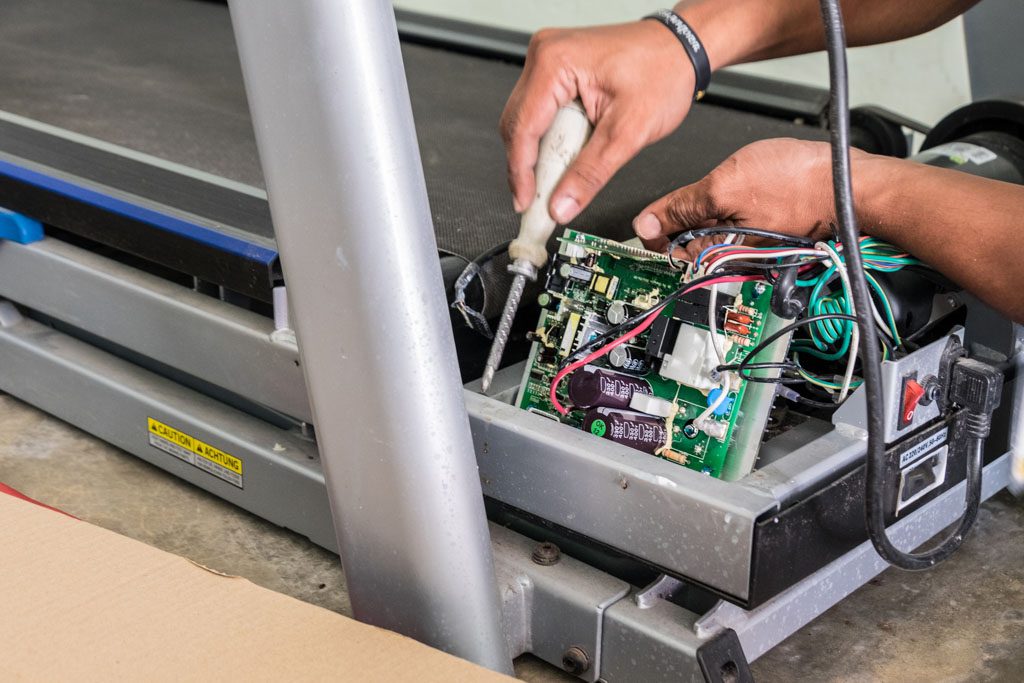 A closeup of a technician using a screwdriver to repair a treadmill.