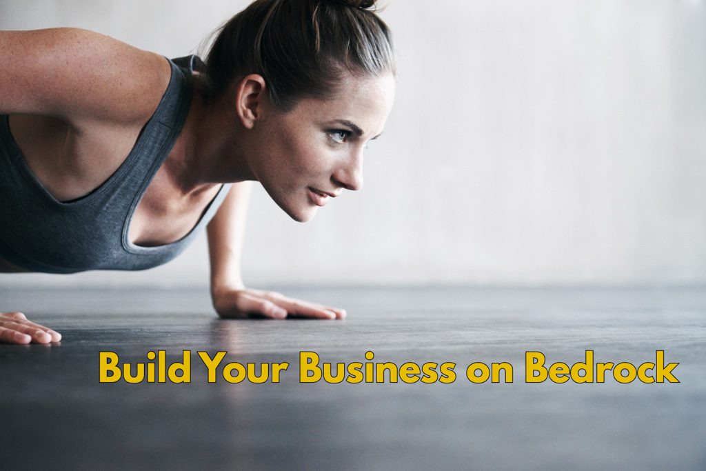A woman does a pushup on a black floor with the label "build your business on bedrock."