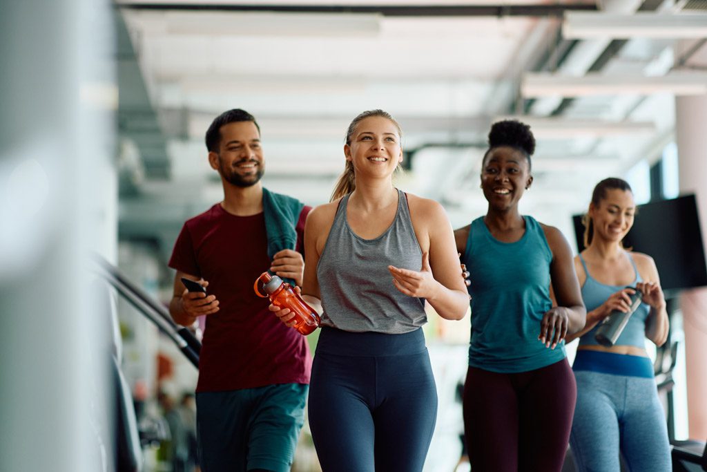 Four smiling clients arrive for a semi-private personal training at a gym.