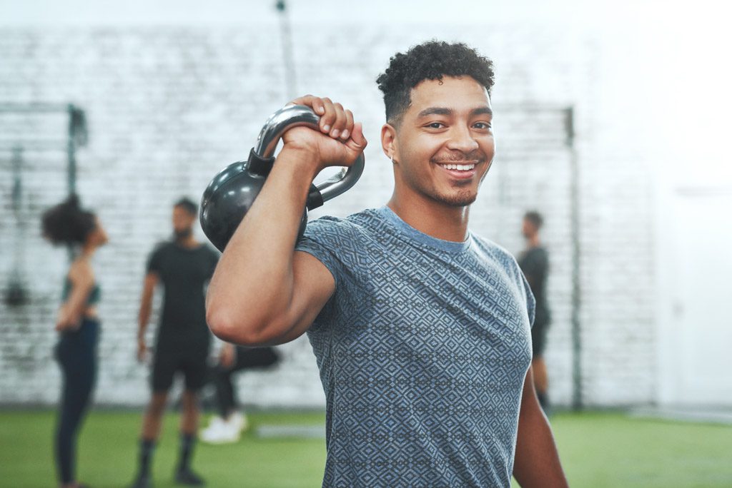 A smiling hopeful gym owner poses with a kettlebell in his gym.