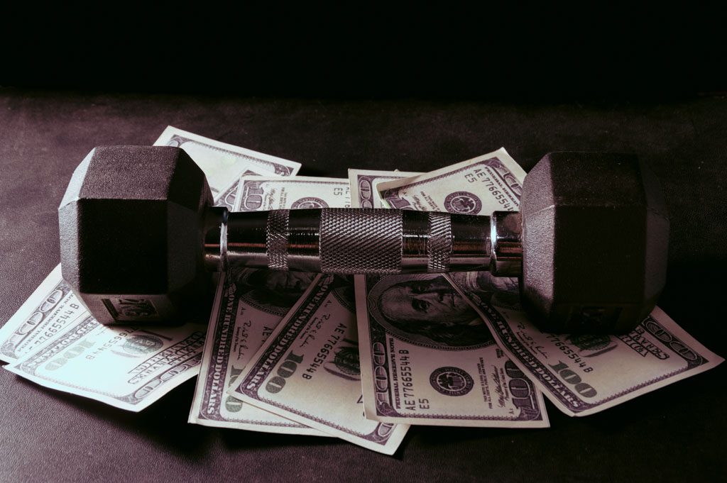 A photo of a dumbbell sitting on U.S. currency.