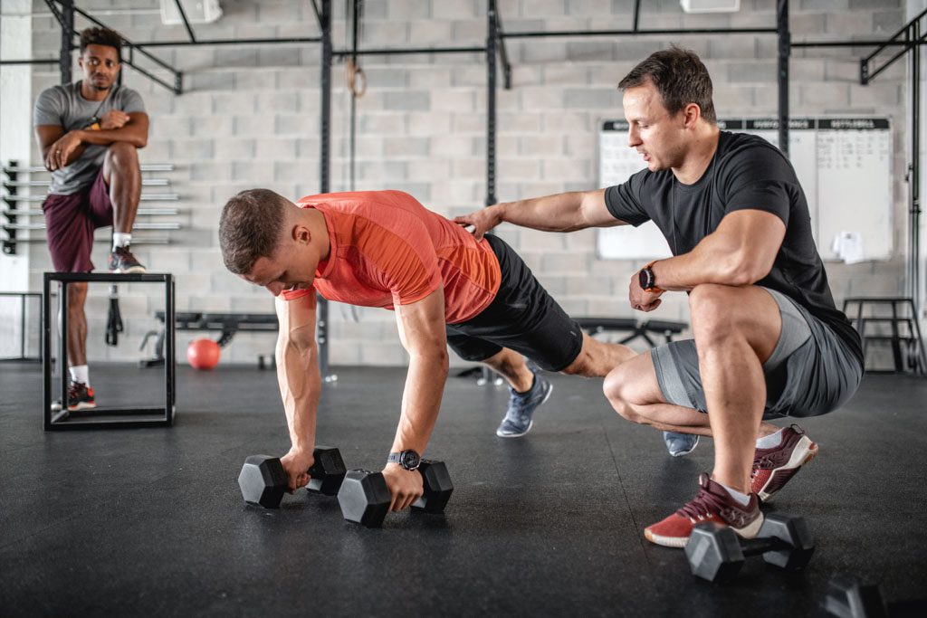 A gym owner coaches a personal training client through a push-up.