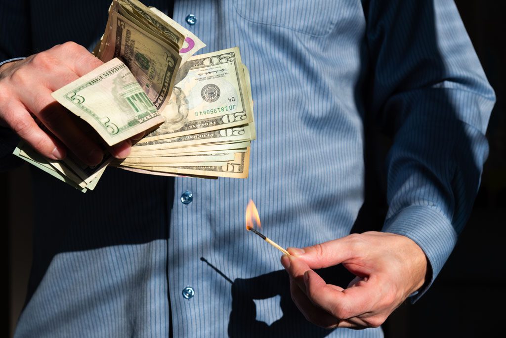 A gym owner holds a lit match beneath a wad of cash.
