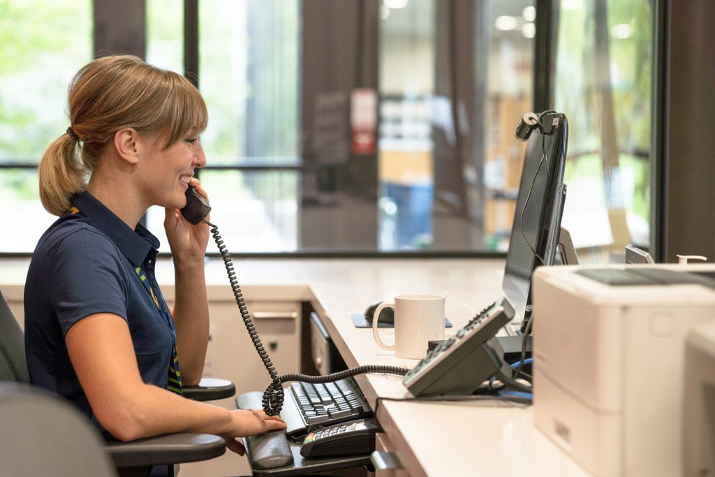 A smiling gym manager answers the phone at the front desk of a gym business.
