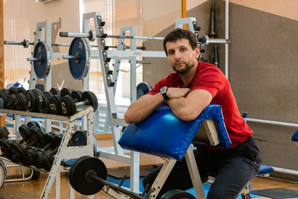 A struggling gym owner sits on a preacher-curl bench and stares off into space.
