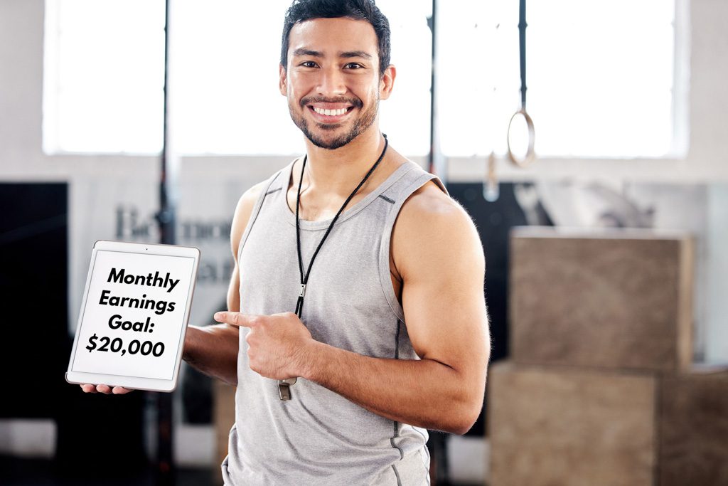 A smiling gym owner holds a tablet with the words "monthly earnings goal: $20,000."
