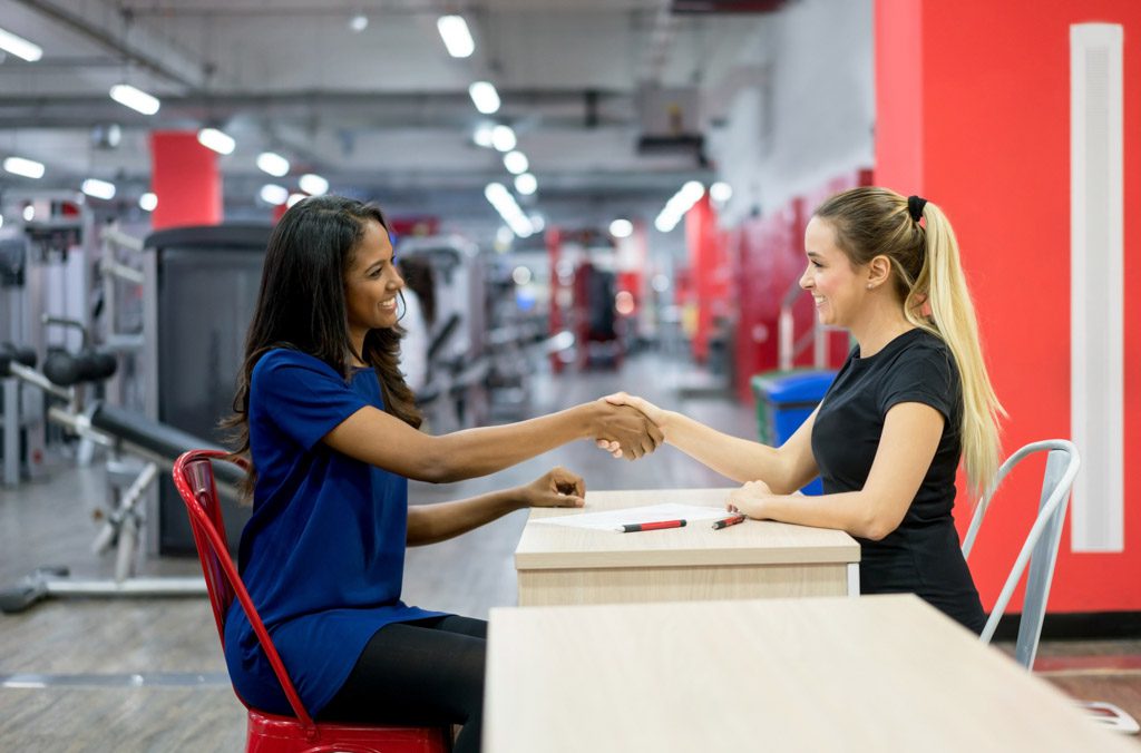A new clients shakes hands with a gym owner after signing up for a membership.