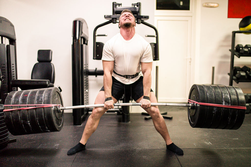 A strong man uses a sumo deadlift to lift 585 lb. in a gym.