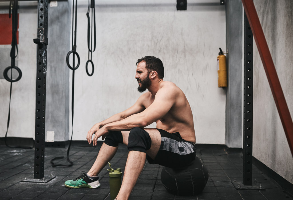 A fit man sits on a medicine ball in a gym.